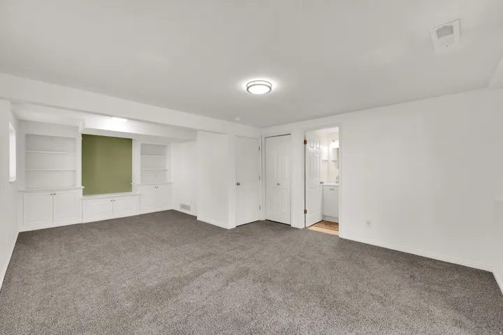 Spacious room featuring neutral carpeting, recessed lighting, built-in white cabinetry with shelving, and a vanity visible through an open doorway