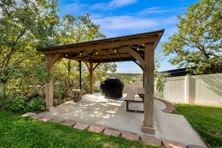 Spacious outdoor patio featuring a wooden gazebo with built-in lighting, concrete hardscaping, and a privacy fence