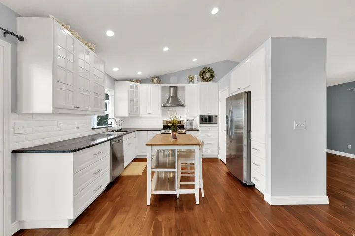 Kitchen featuring white cabinetry, dark countertops, a central island with wood-finish top, stainless steel appliances, and wood-finish flooring