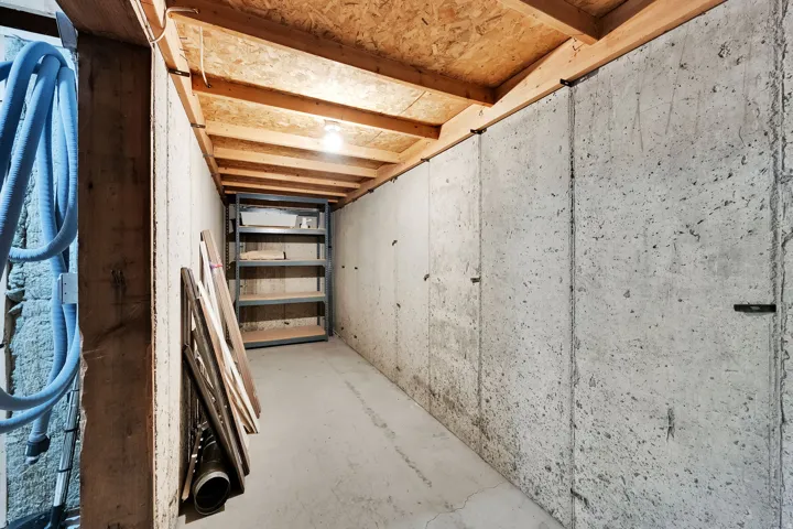 Unfinished concrete walls, concrete floor, exposed wooden ceiling beams, and overhead lighting