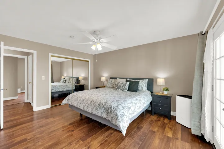 Wood-finish flooring throughout, complemented by a ceiling fan with integrated lighting, and a mirrored closet with sliding doors