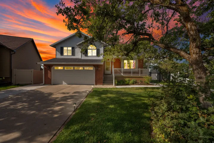 Two-story residence featuring light gray siding, a brick lower level, an attached two-car garage, and a front porch with white railings