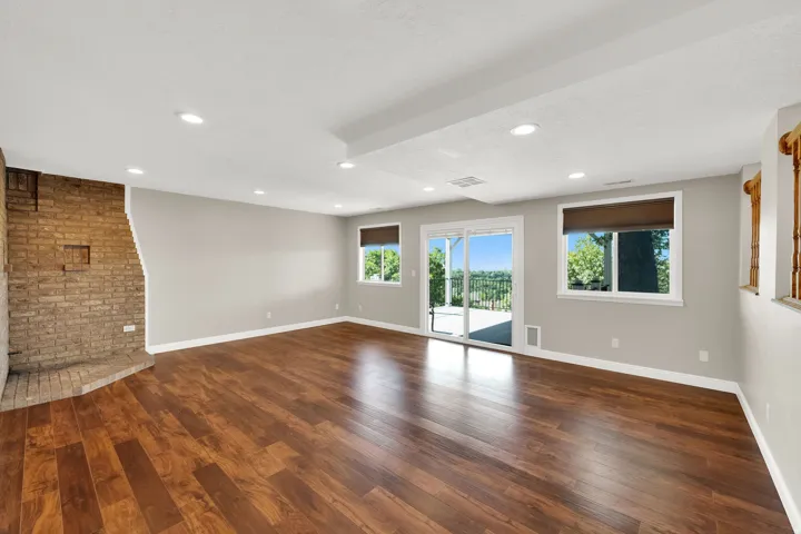 Spacious room featuring wood-finish flooring, a brick-clad fireplace, recessed lighting, and a sliding glass door leading to an outdoor deck