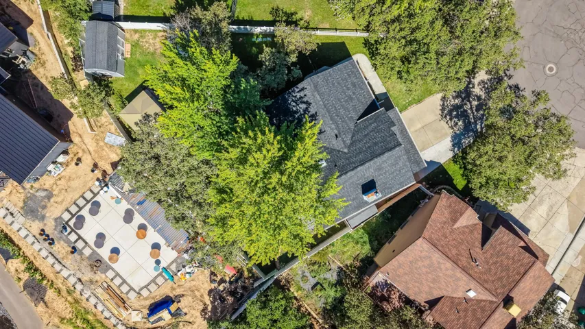 Expansive property featuring a black asphalt shingle roof, mature trees, and a concrete patio