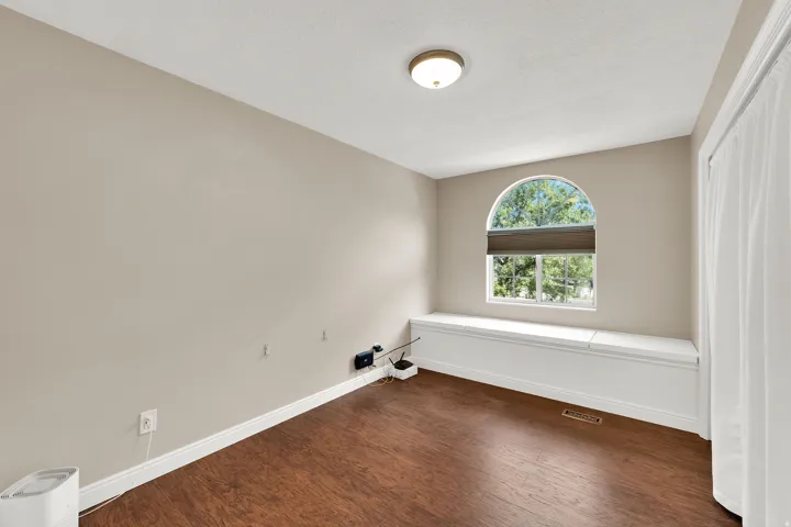 Arch-top window with integrated blind, wood-finish flooring, built-in window bench, ceiling-mounted light fixture, and neutral wall paint