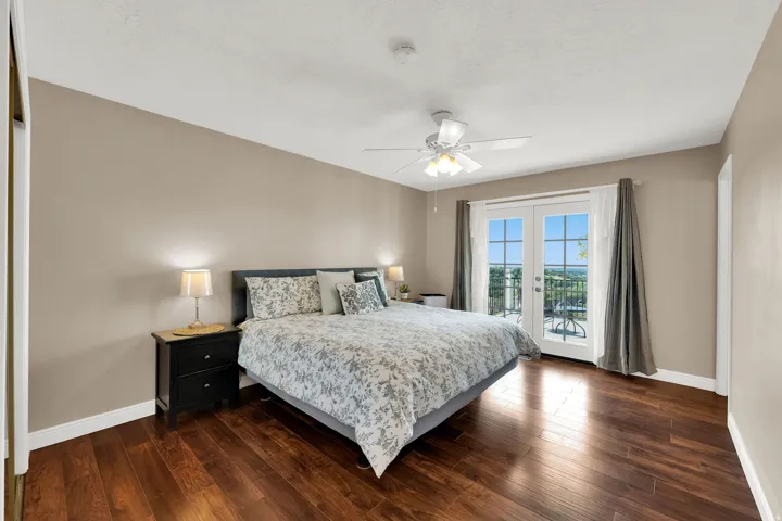 Wood-finish flooring, ceiling fan with integrated lighting, double French doors, and a balcony with black wrought iron railing