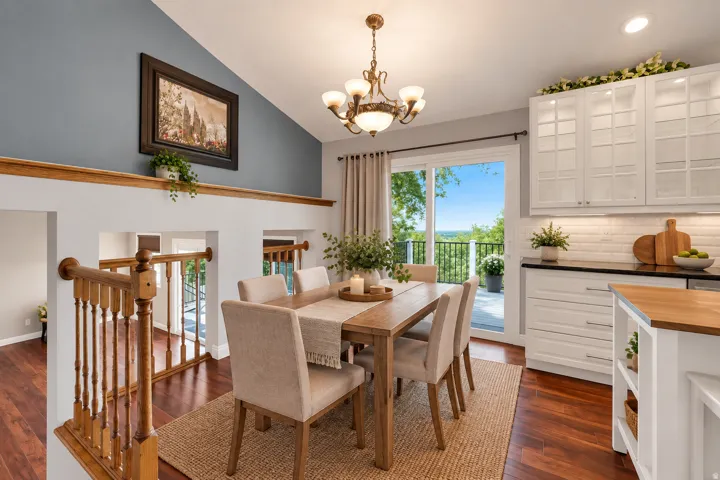 Vaulted ceiling, wood-finish flooring, white cabinetry with glass inserts, sliding glass door, and a wooden railing