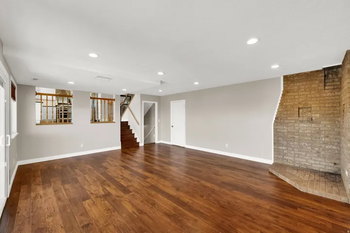 Spacious room featuring wood-finish flooring, a brick fireplace, recessed lighting, and a staircase with wood railings