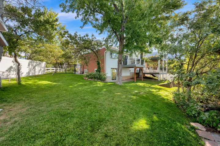 Expansive sloped lawn with mature trees, multi-level deck, and clear panel railings