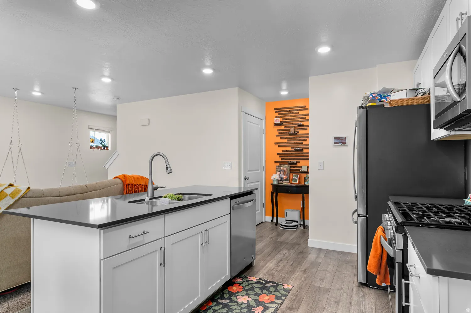 Kitchen with white cabinetry, black countertops, stainless steel appliances, and wood-finish flooring