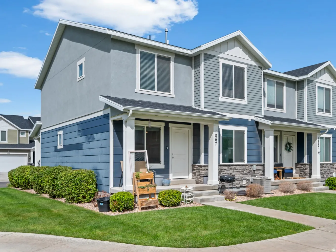 Townhome exterior featuring multi-toned siding, stone veneer accents, a covered front porch, and a manicured lawn
