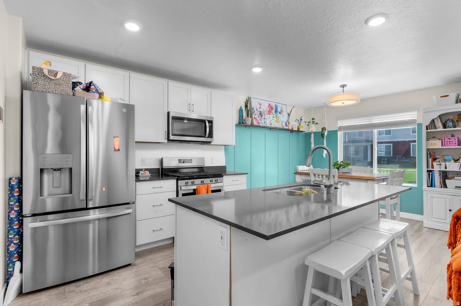 Kitchen featuring white cabinetry, stainless steel appliances, a center island with a sink, and wood-finish flooring