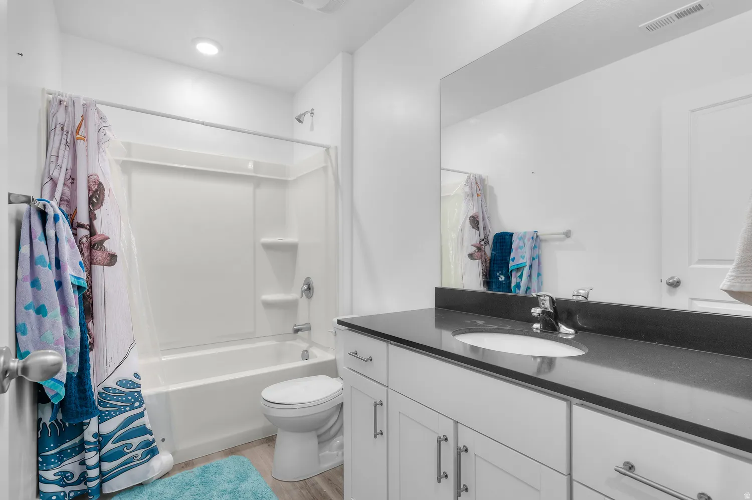 White vanity with cabinet storage, dark countertop, and integrated sink
