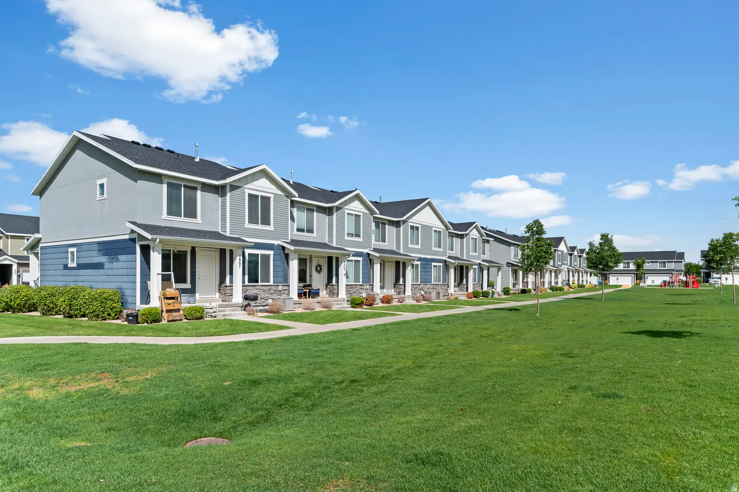 Row of residential townhomes featuring two-tone siding, dark roofs, and covered entryways with columns