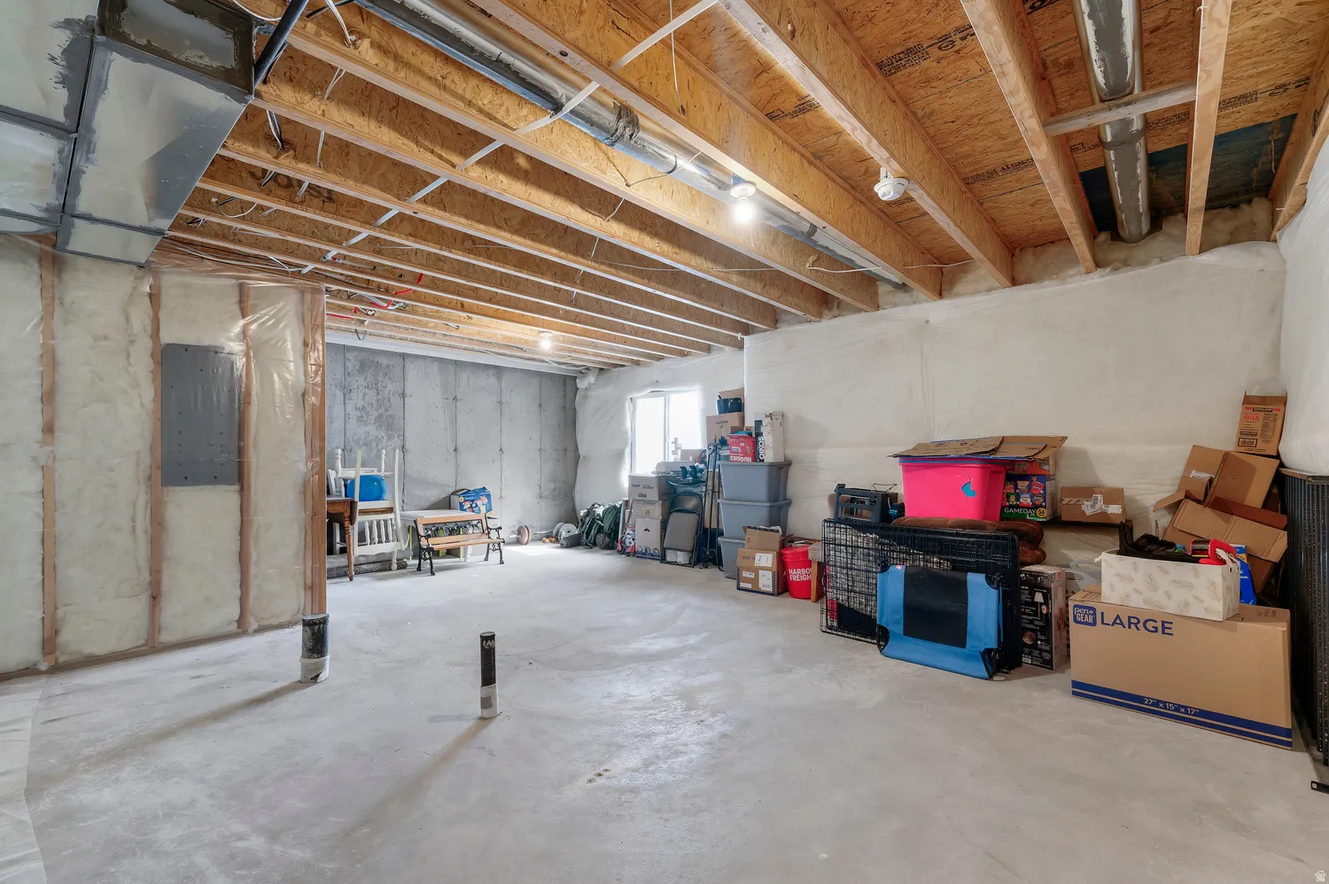 Unfinished basement featuring exposed wood joists, concrete flooring, and a window