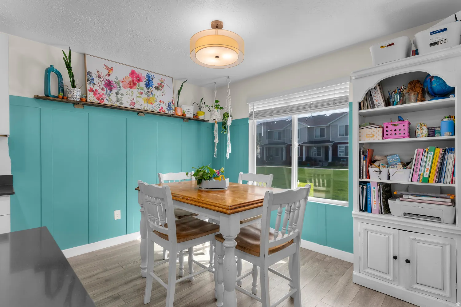 Wood-finish flooring with a wood-top dining table, white chair seating, and a built-in white bookshelf