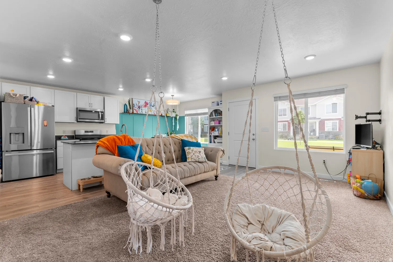 Open-concept living space with recessed lighting, wood-finish flooring, and a kitchen featuring white cabinetry and black countertops
