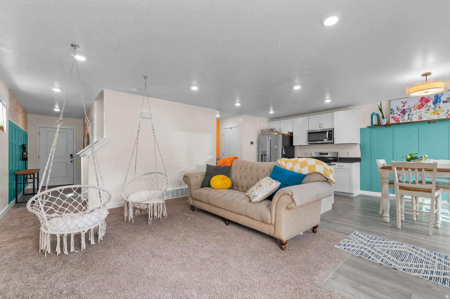 Open-concept living area with recessed lighting, wood-finish flooring, and white kitchen cabinetry with stainless steel appliances