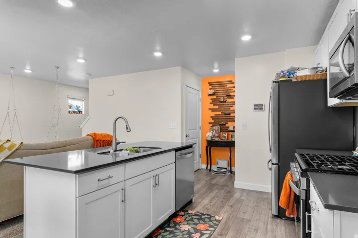 Kitchen with white cabinetry, black countertops, stainless steel appliances, and wood-finish flooring