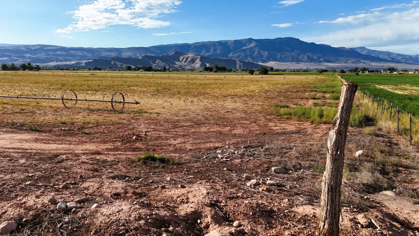 Expansive open terrain with natural vegetation, bordered by a wire fence and a wooden post
