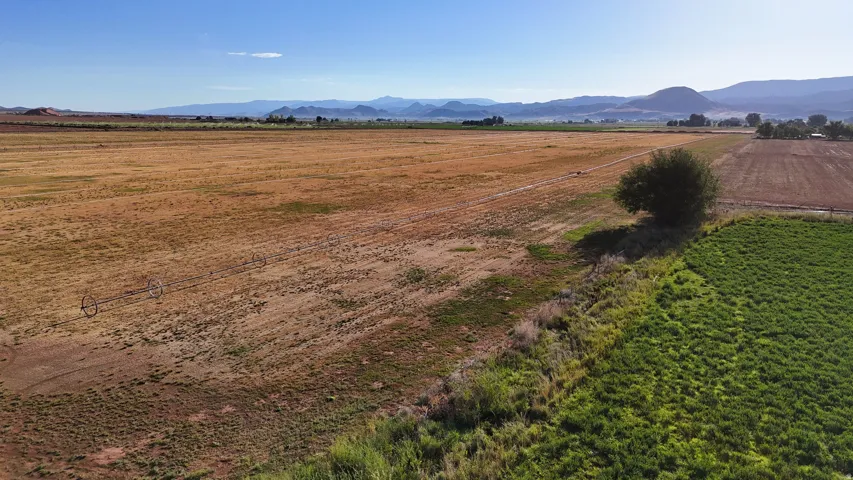 Expansive agricultural land featuring a mix of cultivated and uncultivated fields, with distant mountains providing a scenic backdrop