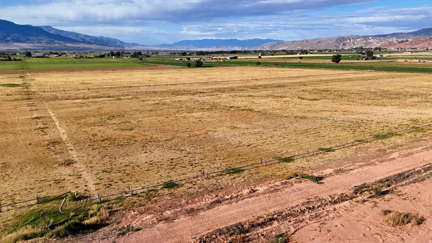 Expansive open land with distant mountain ranges, a partial wire fence, and an unpaved road