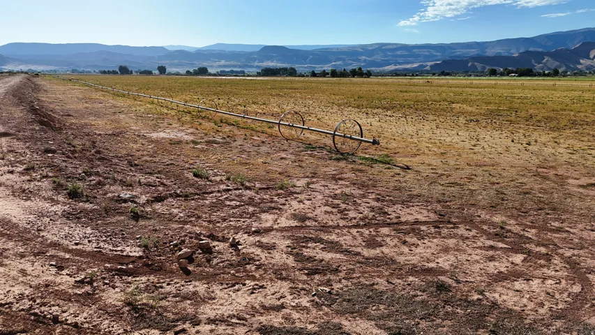 Expansive agricultural land featuring a wheel-line irrigation system and distant mountains