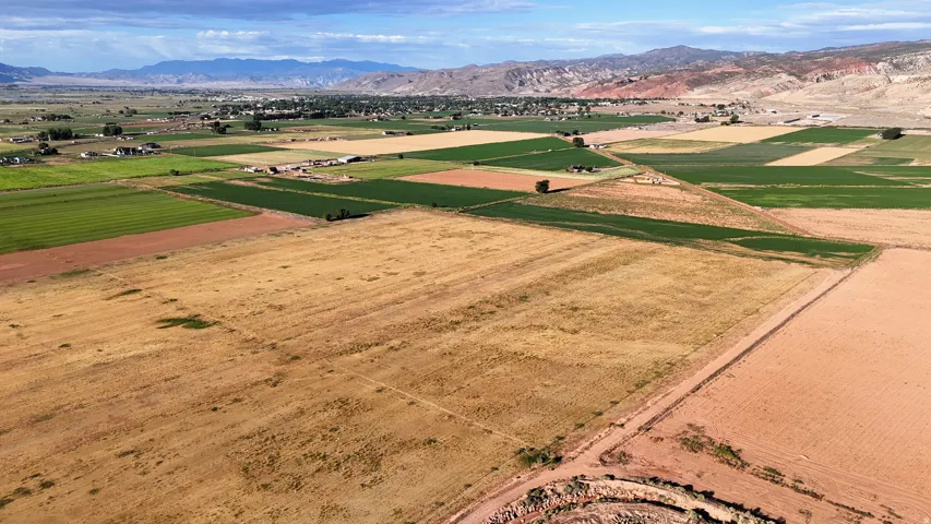 Expansive agricultural landscape with varied crop fields, distant mountain range, and scattered rural structures