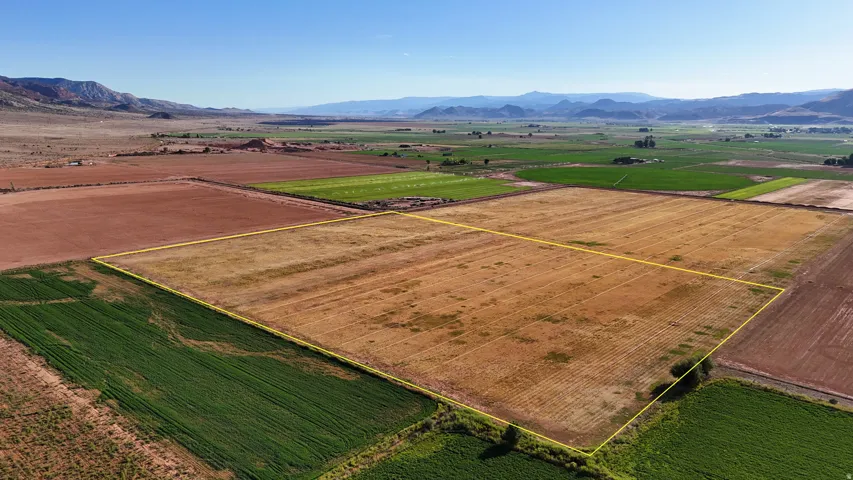 Expansive land parcel featuring clear boundaries, surrounding agricultural fields, distant mountains, and a clear sky