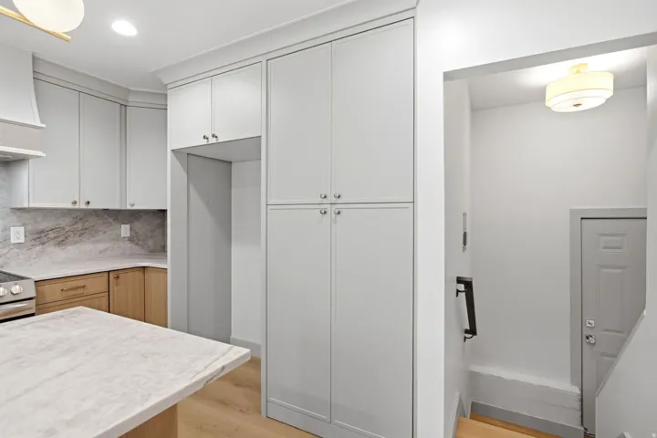 Light-toned wood-finish flooring, light grey cabinetry, stone countertops, stainless steel range, and a ceiling-mounted light fixture