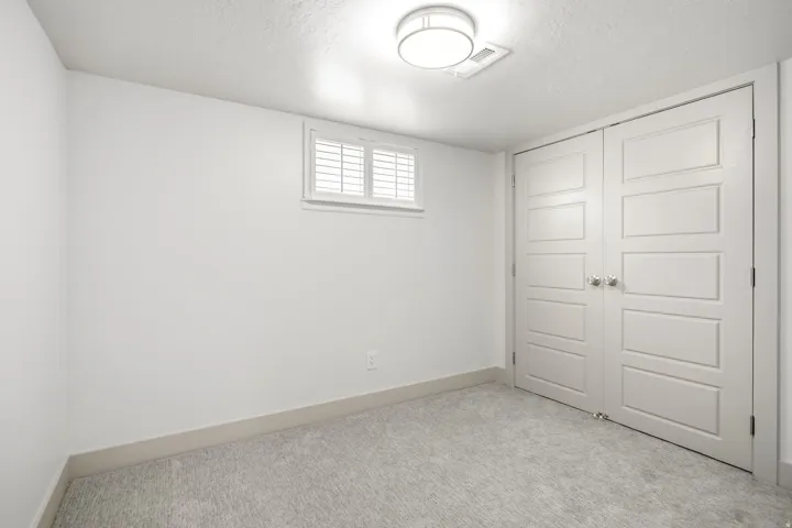 White painted walls and ceiling, wall-to-wall carpeting, window with internal shutters, ceiling-mounted light fixture, and double paneled doors with round hardware