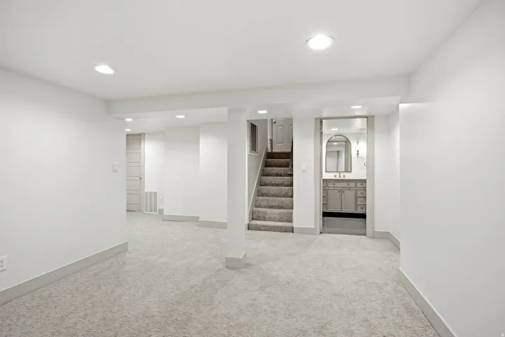 Carpeted lower level with recessed lighting, a staircase with carpeted treads, and a bathroom featuring a vanity with a rectangular sink and an arched mirror