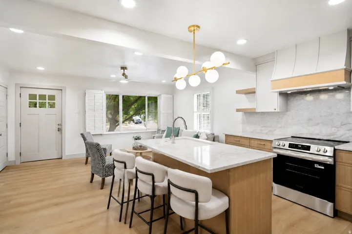 Kitchen featuring a central island, light wood-finish flooring, white shaker-style cabinetry, a stainless steel range, and a white tile backsplash
