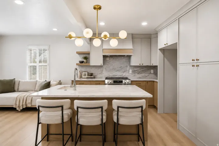 Kitchen featuring a large center island with integrated sink, panel-front cabinetry, wood-finish flooring, and a decorative linear chandelier