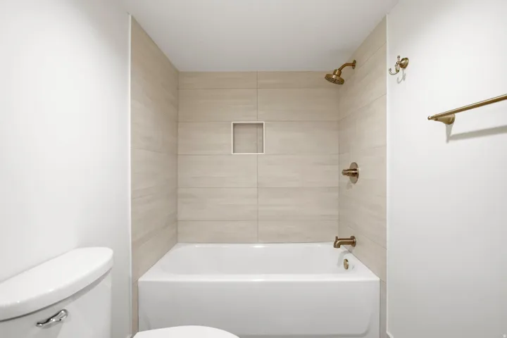 White bathtub with integrated shower, tiled surround, and bronze fixtures