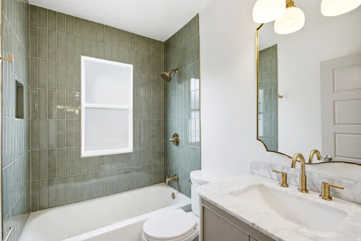 Subway tile shower surround, white bathtub, vanity with integrated sink, gold-finish faucet, and an ornate mirror