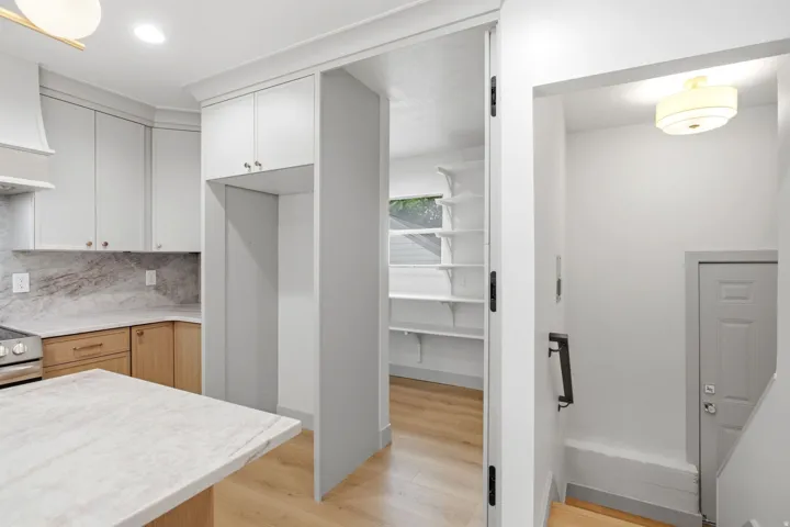 Kitchen featuring light-toned cabinetry, light stone countertops, integrated range hood, and a pantry with built-in shelving