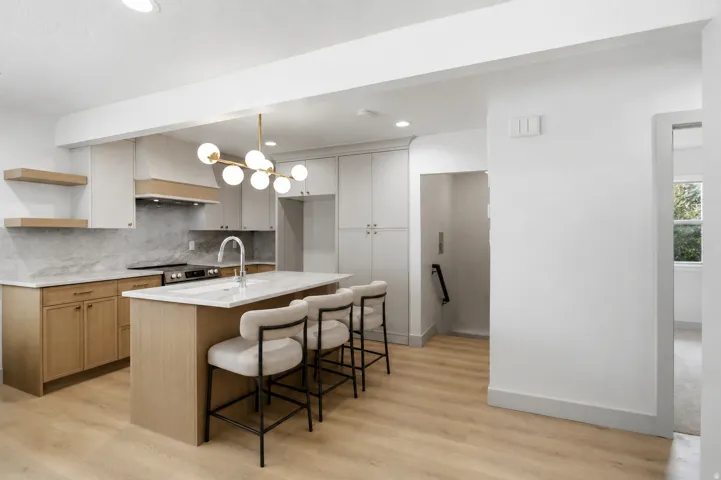 Modern kitchen with two-tone cabinetry, a central island featuring a sink, stainless steel appliances, and wood-finish flooring