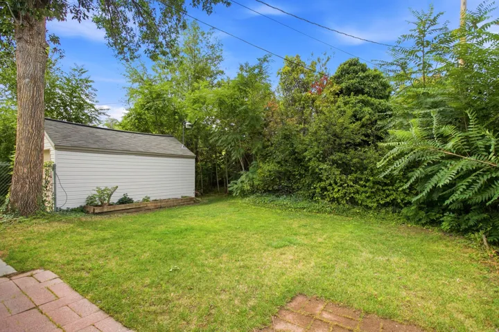 Expansive lawn area with a white detached shed, mature trees, and natural landscaping