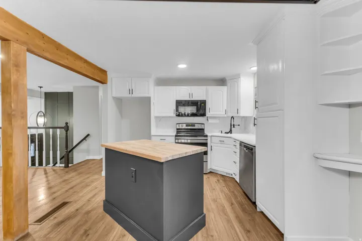 Kitchen featuring a central island with wood countertop, white cabinetry with dark hardware, stainless steel appliances, and wood-finish flooring