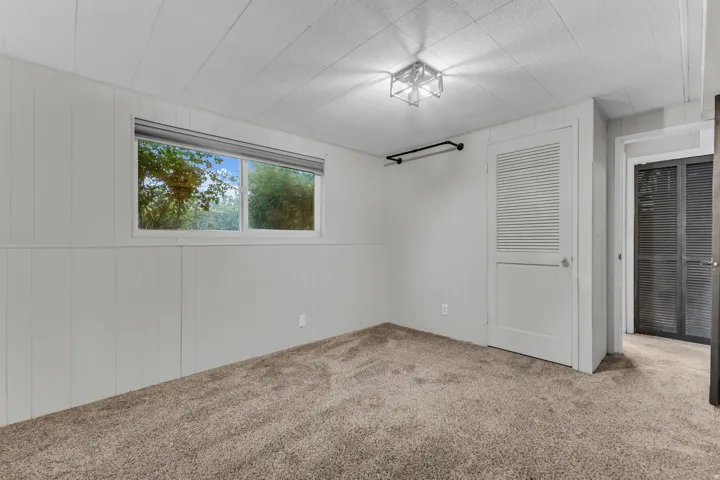 Wall-to-wall carpeting, paneled walls, and a single window with roller shade