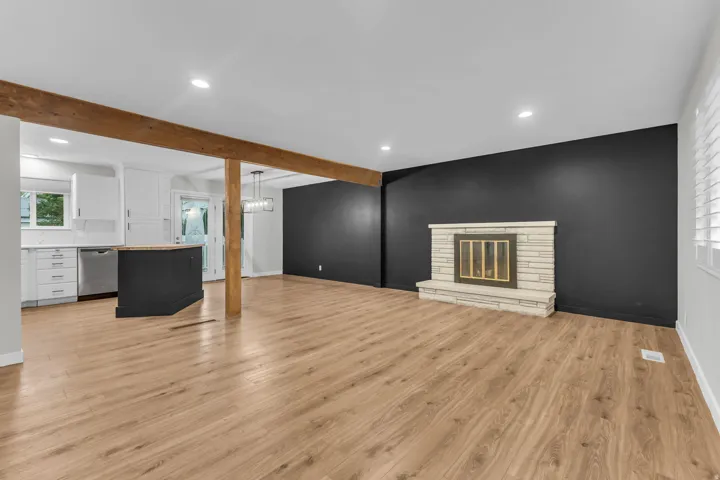 Open-concept living space featuring wood-finish flooring, exposed wood beams, and a stone-clad fireplace
