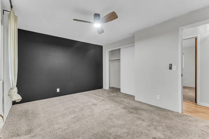 Carpeted room with a ceiling fan, a dark accent wall, and a sliding closet door