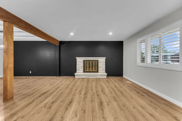 Recessed lighting, wood-finish flooring, exposed wood beam, stone-clad fireplace with brass insert, and a window with plantation shutters