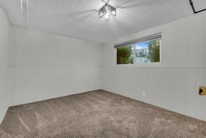 Carpeted room featuring white paneled walls, a window with horizontal blinds, and a flush-mount ceiling light fixture