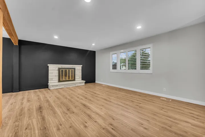 Wood-finish flooring throughout, light-colored walls, recessed lighting, and a stone-clad fireplace with hearth
