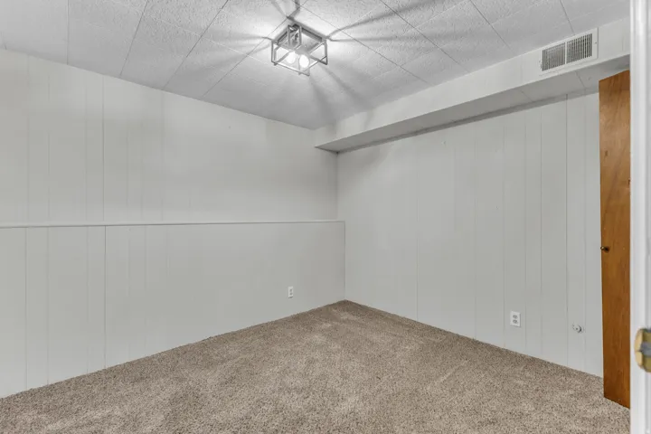 Carpeted room featuring white vertical paneling and a drop ceiling with recessed lighting
