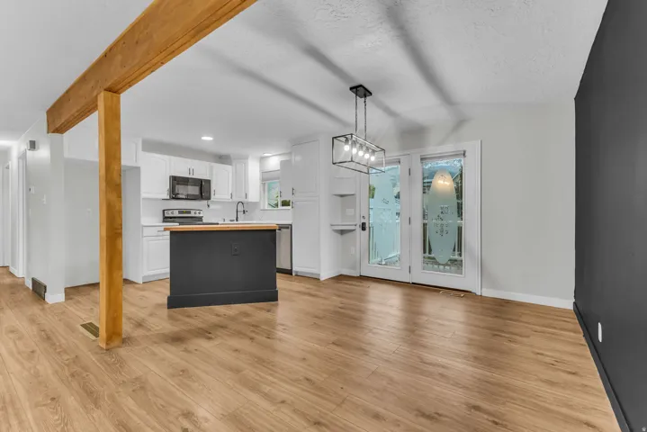 Wood-finish flooring, exposed wood beam, white cabinetry, integrated kitchen island with wood countertop, and French patio doors