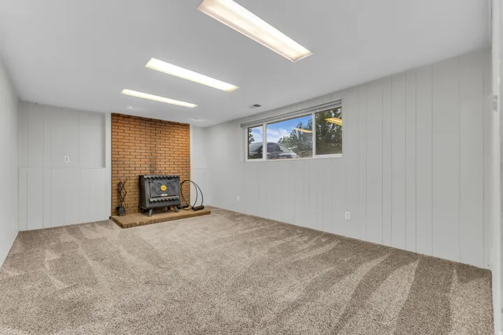 Spacious room featuring a brick accent wall, a cast iron stove, wall-to-wall carpeting, and a large window