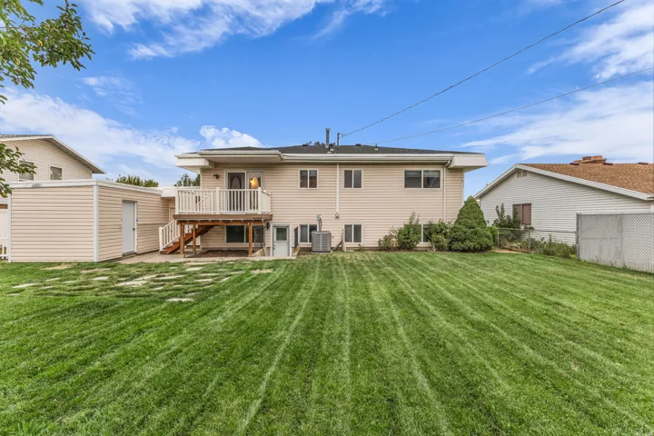 Expansive green lawn with stepping stones, featuring a rear deck with white railings, and a detached storage shed